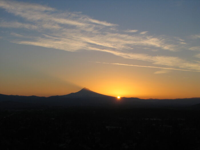 Sun rises to the south of Mount Hood as seen from Rocky Butte. The mountain casts a shadow to the north.