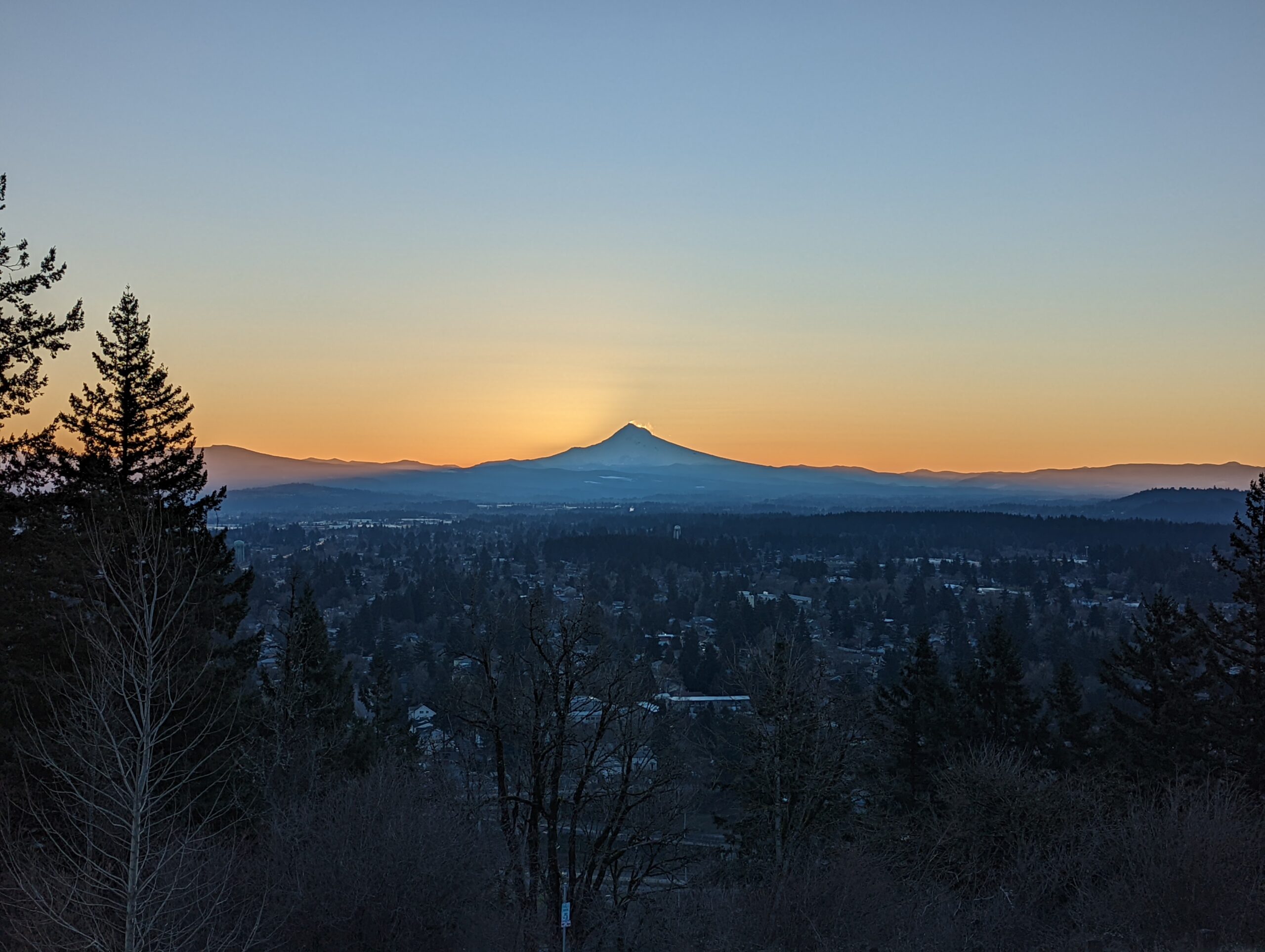 Mount Hood as seen from Rocky Butte before sunrise. The sun is starting to appear in the wind-blown snow from the summit.