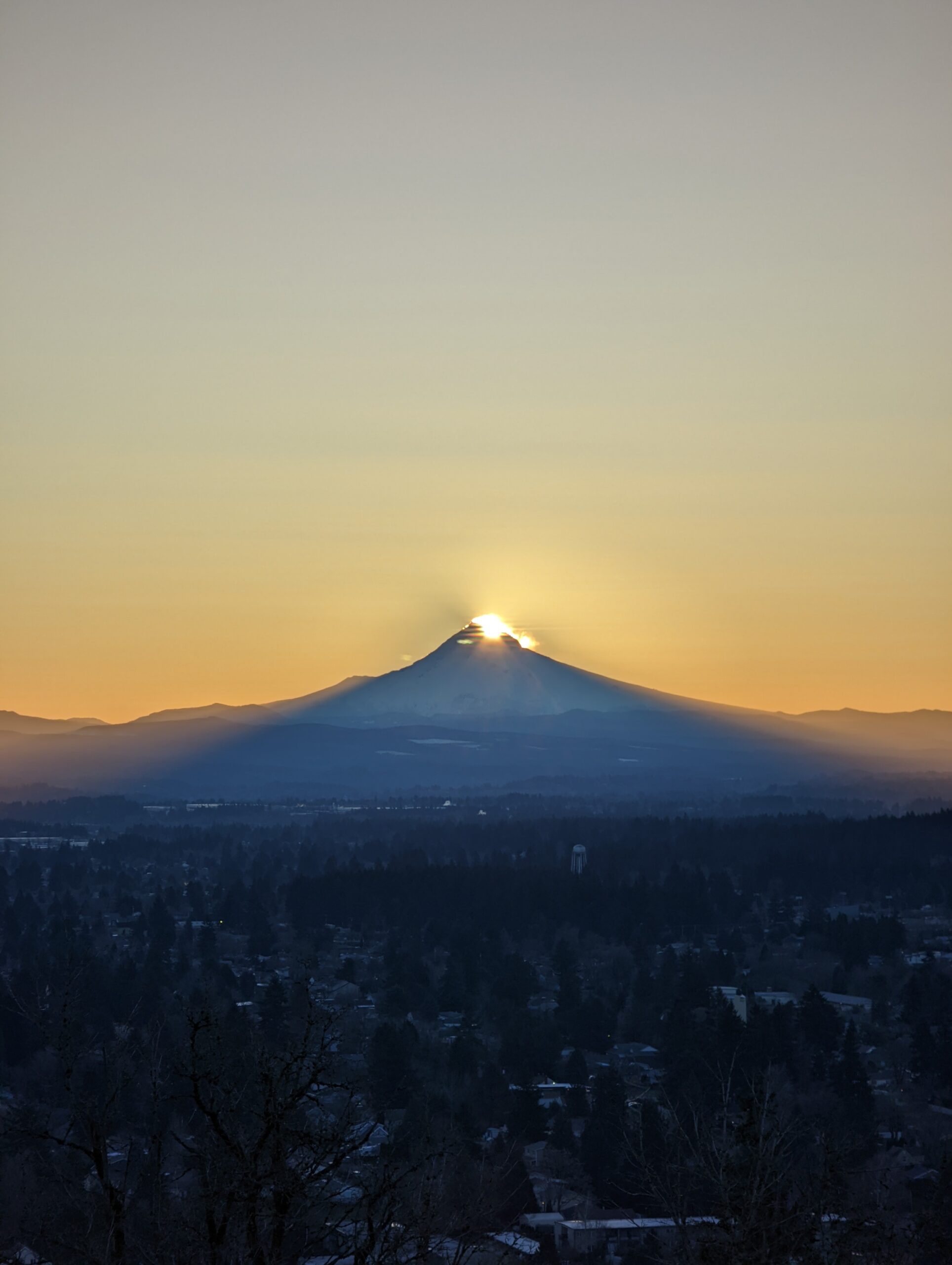 The sun is appearing from behind the summit of Mount Hood with the shadow cast on the city.