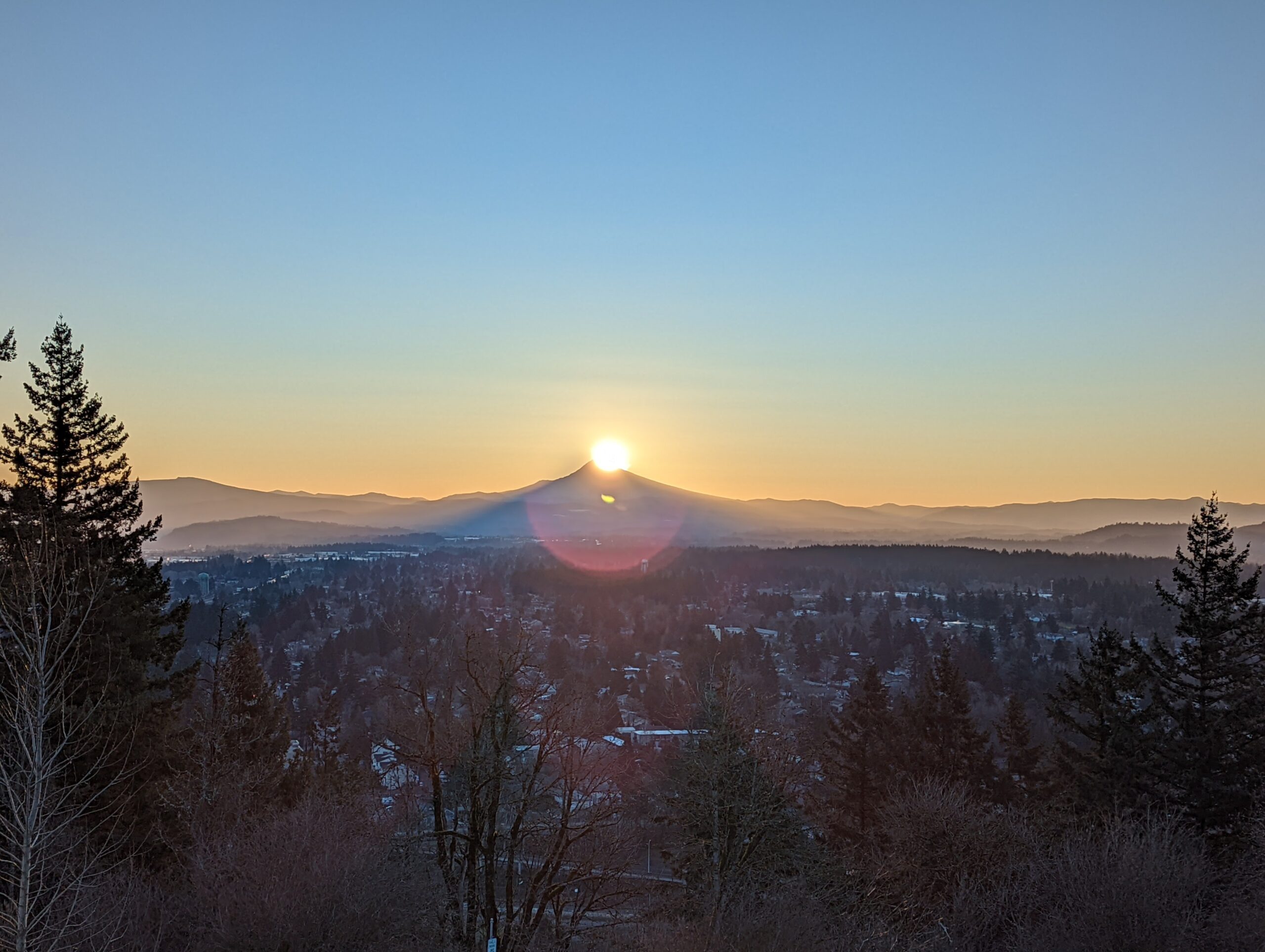 The sun has risen from behind the summit of Mount Hood with a lene flair encircling the mountain.